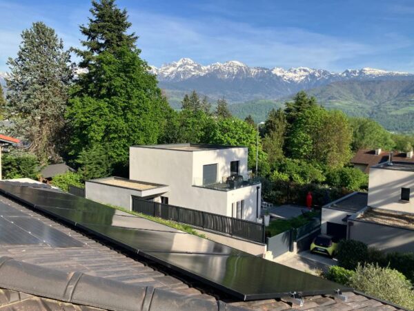 Un installateur photovoltaique a mis des panneaux solaires sur un toir maison carrée avec les montagnes enneigées en fond.