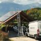 Un abri voiture avec montagne en arrière plan équipé de panneaux solaires, avec le camion blanc d'Alpesphotons.